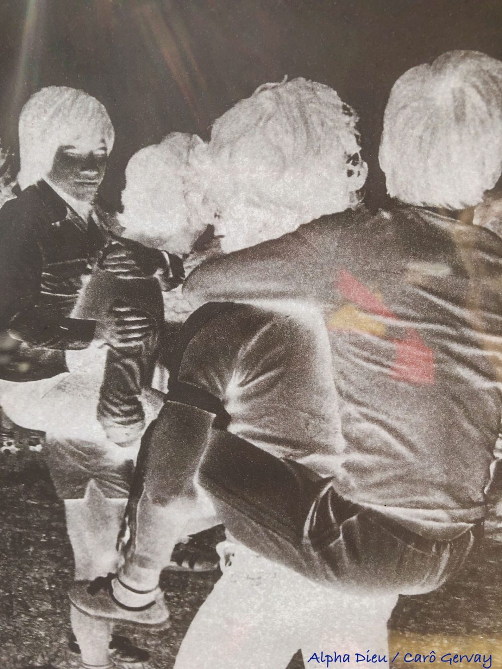 Photographing a digitally printed paper negative from a photograph taken by Alpha Dieu in 1977. The sun beams enter the frame which in turn helps the window reflect my yellow shirt and red darkroom apron. Photo: Carô Gervay, May 2025.